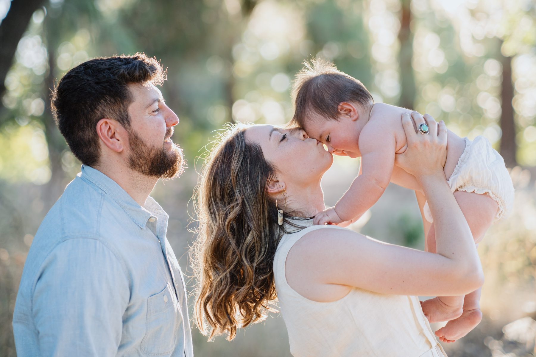 Mom kissing baby while dad watches in golden light
